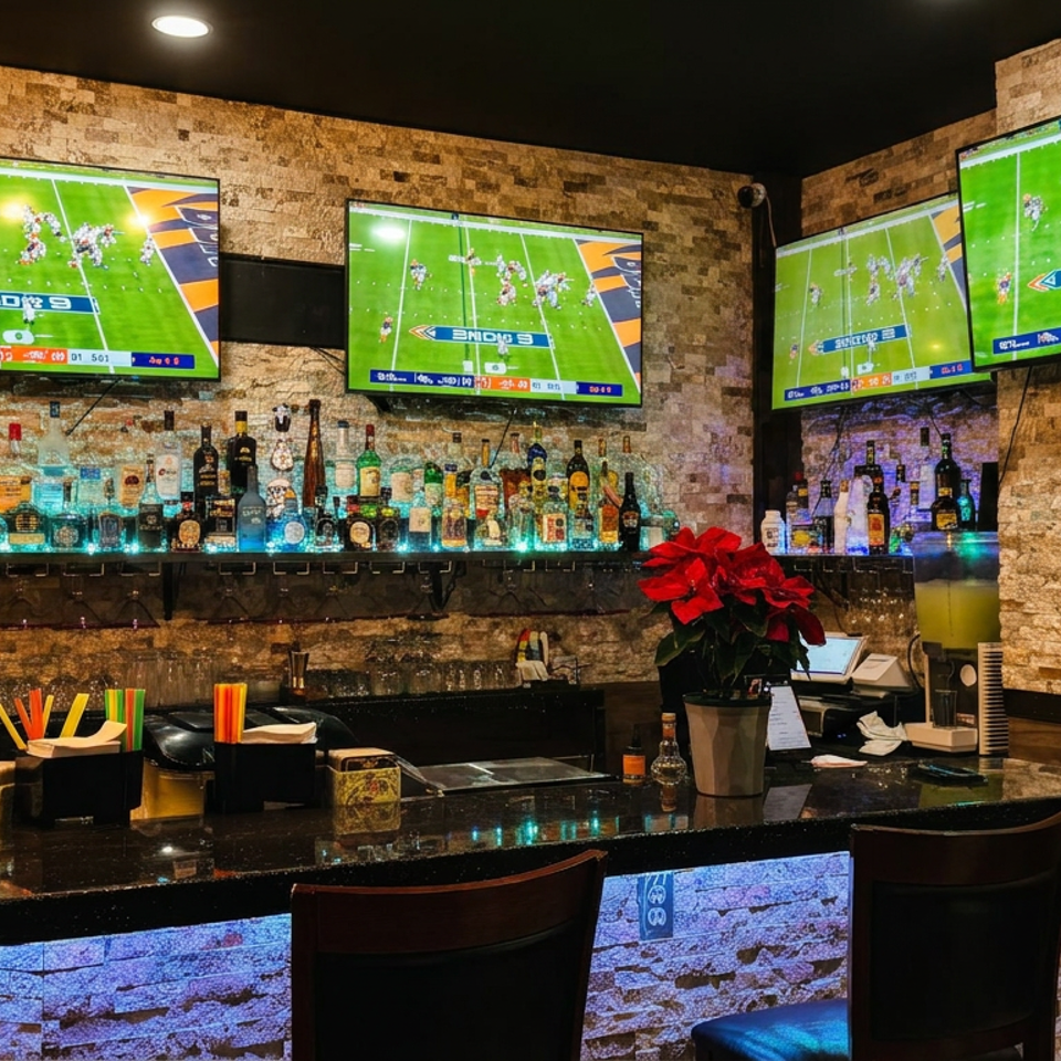 Sports bar interior with four televisions showing football, illuminated liquor shelves, black bar counter, stools, and red poinsettias.